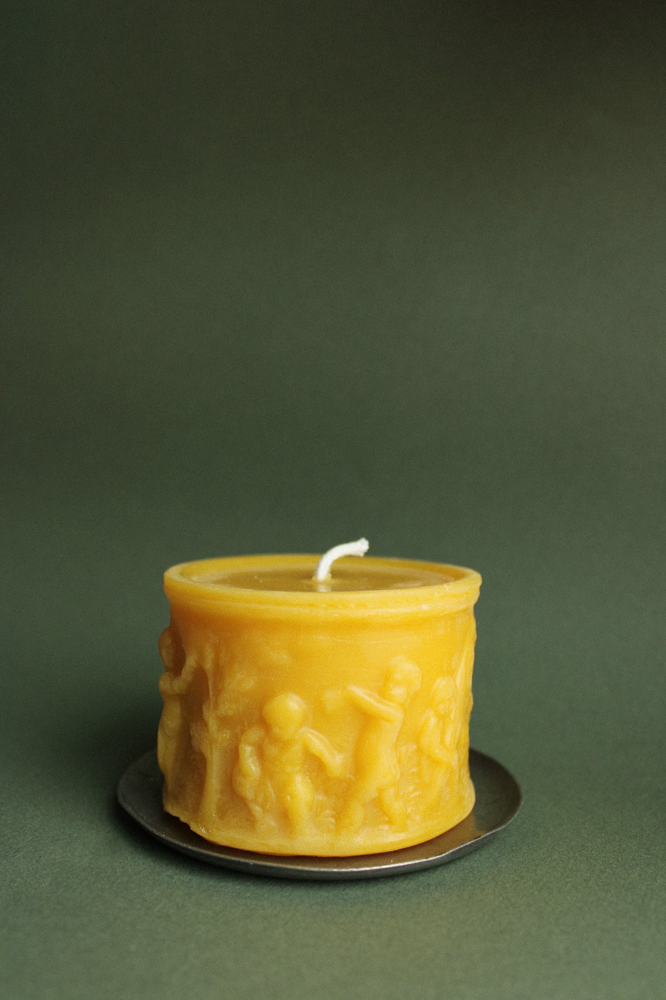 100% beeswax pillar candle in front of a forest green backdrop. The candle features a scene of angelic children gardening. 